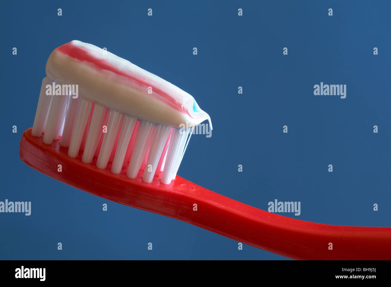 Nahaufnahme von gestreifte Zahnpasta auf roten Zahnbürste blau Hintergrund Stockfoto