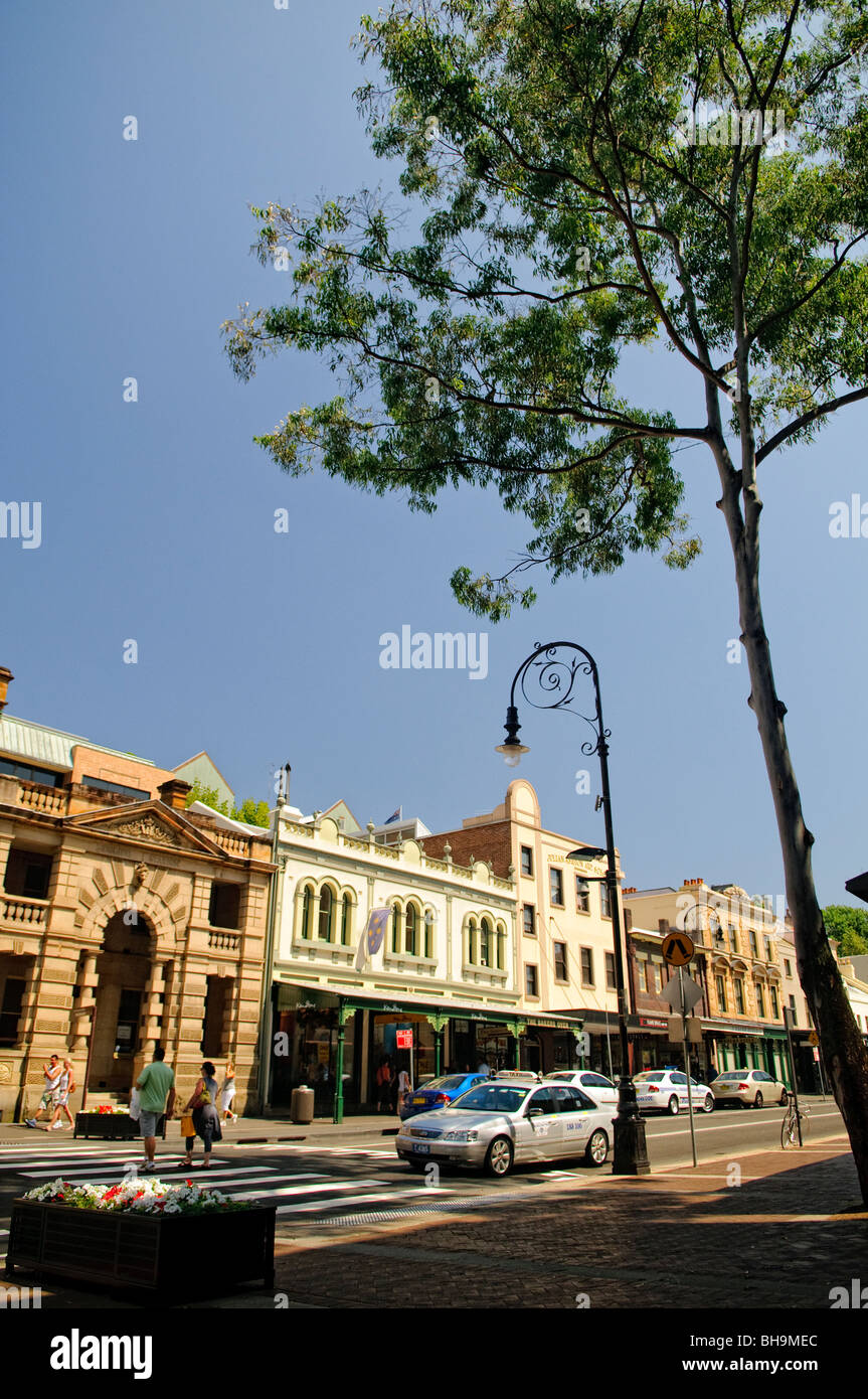 The Rocks Historic District George Street Sydney Australien // SYDNEY, Australien – historische Geschäfte säumen die George Street im Rocks District der Innenstadt von Sydney. Dieses denkmalgeschützte Viertel, das 1788 als Ort der ersten europäischen Siedlung Australiens gegründet wurde, verfügt über erhaltene Gebäude aus der Kolonialzeit mit markanten Sandsteinfassaden, die heute Boutiquen, Galerien, Restaurants und Souvenirläden beherbergen. Die Rocks behalten ihren historischen Charakter mit kopfsteingepflasterten Gassen und viktorianischer Architektur und fungieren gleichzeitig als beliebtes Shopping- und Touristenziel in der Nähe des Hafens von Sydney, des Opernhauses, Stockfoto