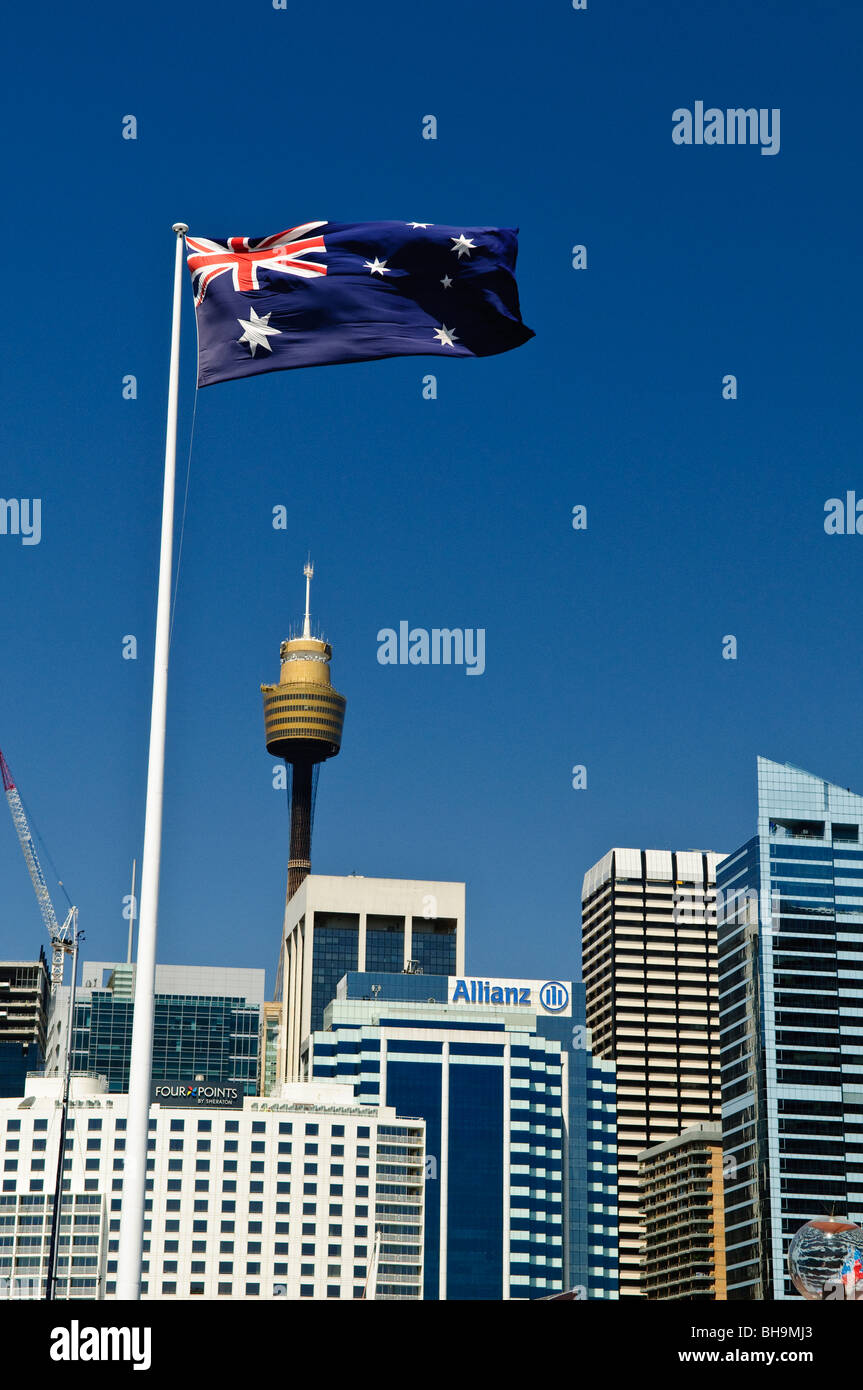 Australian Flag Sydney Centrepoint Tower Sydney // SYDNEY, Australien – eine australische Flagge fliegt stolz im Wind vor einem klaren blauen Himmel, mit Sydneys ikonischem Centrepoint Tower und anderen modernen Gebäuden des Central Business District (CBD) im Hintergrund. Das pulsierende Stadtbild unterstreicht die geschäftige urbane Umgebung von Australiens größter Stadt. Stockfoto