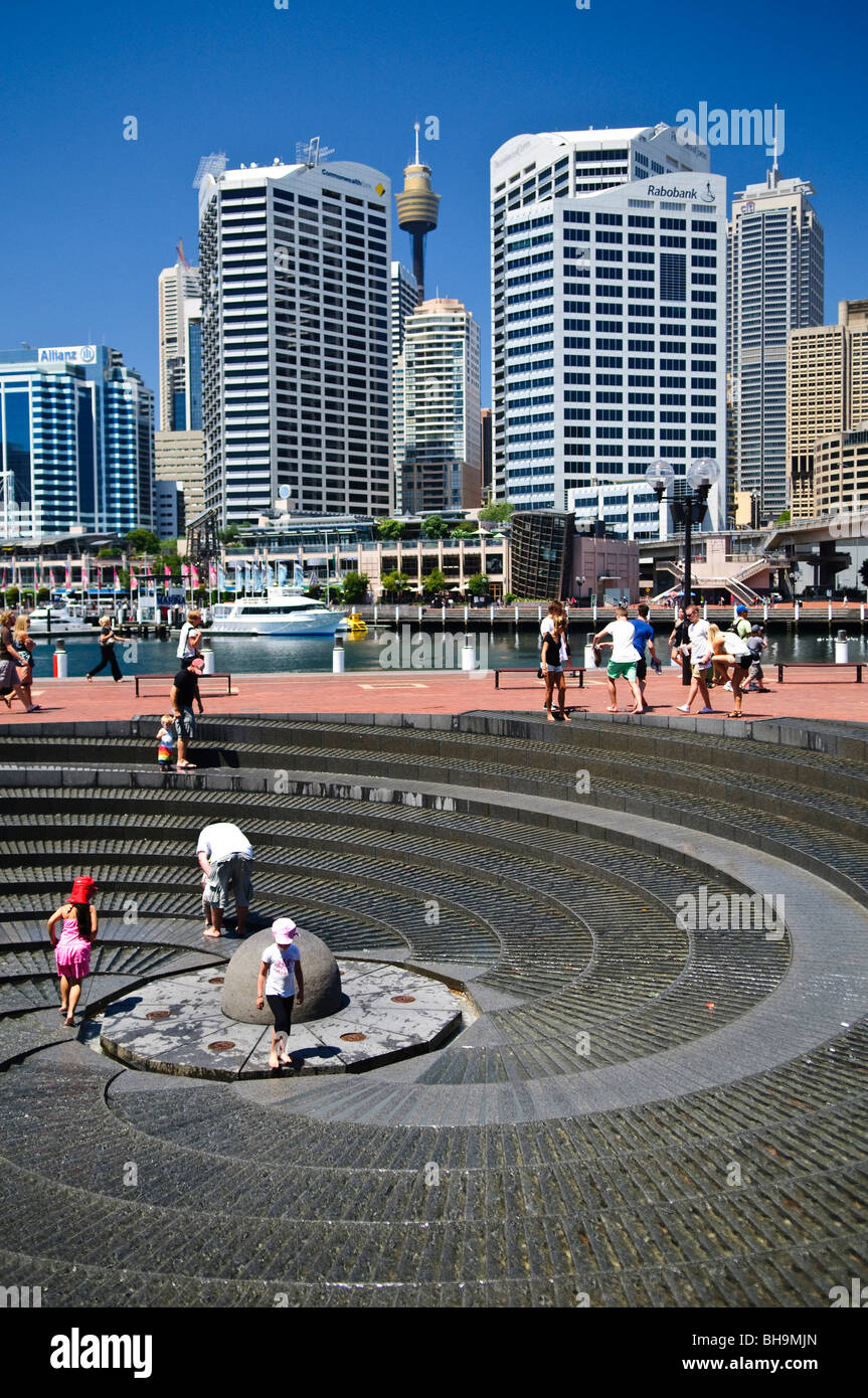 Darling Harbour Spiral Fountain Kinder spielen Sydney // SYDNEY, Australien - Kinder spielen an einem heißen Sommertag im Spiralbrunnen in Darling Harbour. Der berühmte Sydney Tower und die modernen Wolkenkratzer bieten eine lebendige Kulisse für das erfrischende Wasserspiel an diesem beliebten Reiseziel am Wasser. Stockfoto
