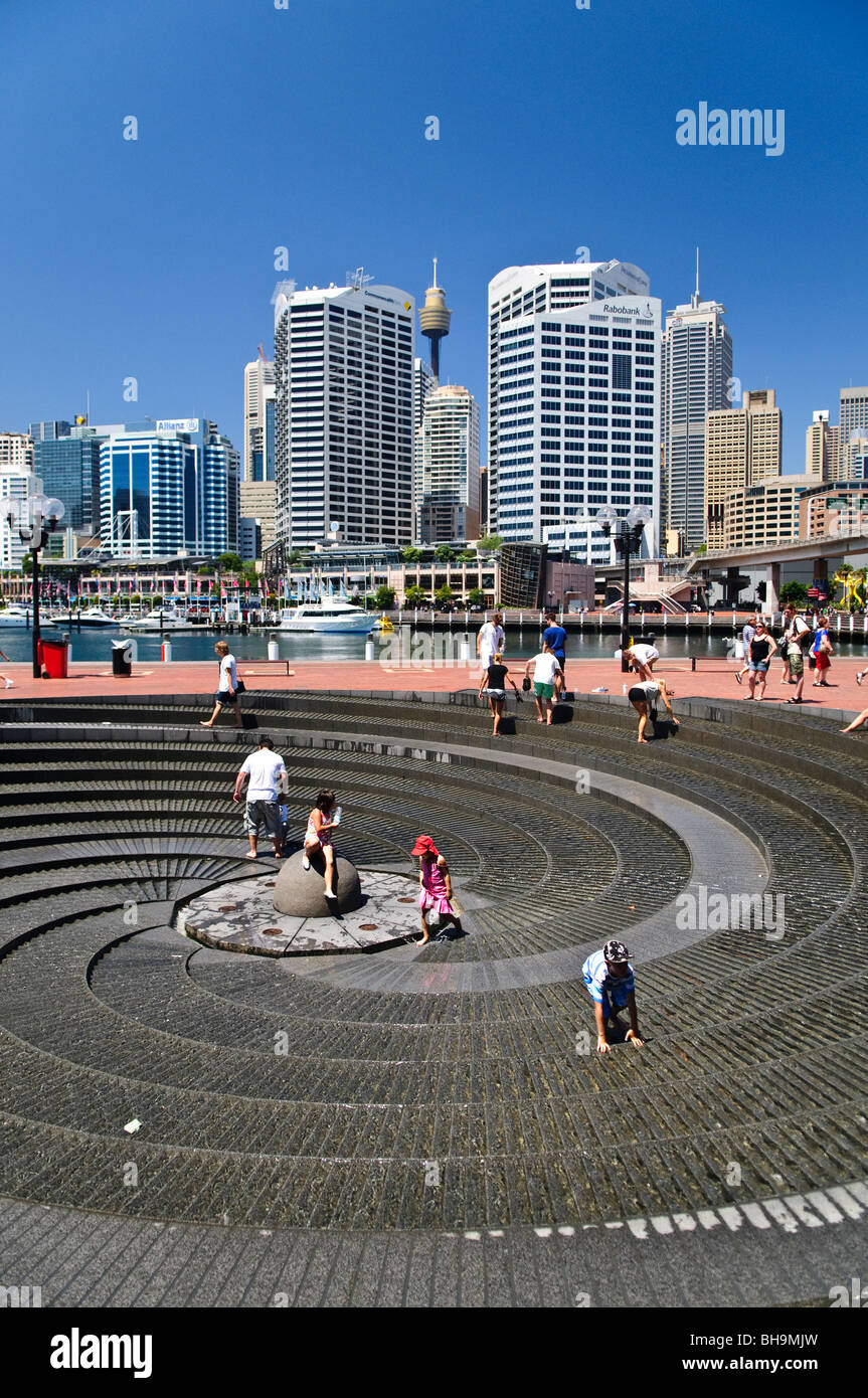 Darling Harbour Spiral Fountain Kinder spielen Sydney // SYDNEY, Australien - Kinder spielen an einem heißen Sommertag im Spiralbrunnen in Darling Harbour. Das berühmte Sydney Tower Eye und die modernen Wolkenkratzer bilden eine beeindruckende Kulisse für die lebhafte Hafenszene. Stockfoto