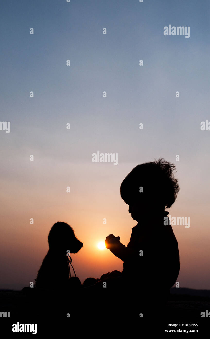 Kleiner Junge sitzt gegenüber seinen Teddy bei Sonnenuntergang. Silhouette. Indien Stockfoto