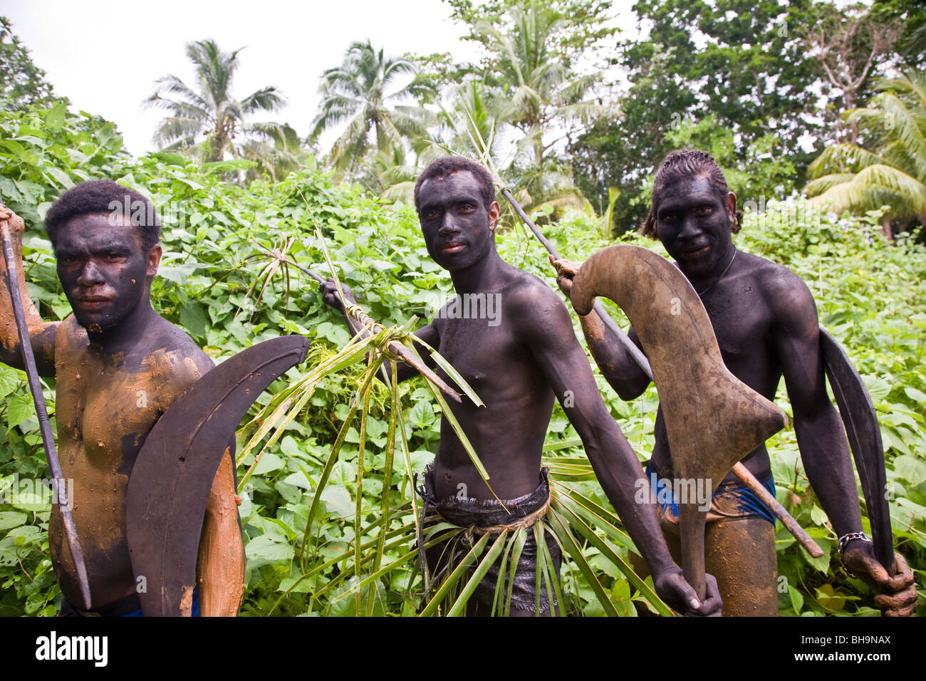 Drei melanesischen Männer posieren für die Kamera trägt traditionelle Schlamm und Kostüme und traditionelle Waffen hält Stockfoto