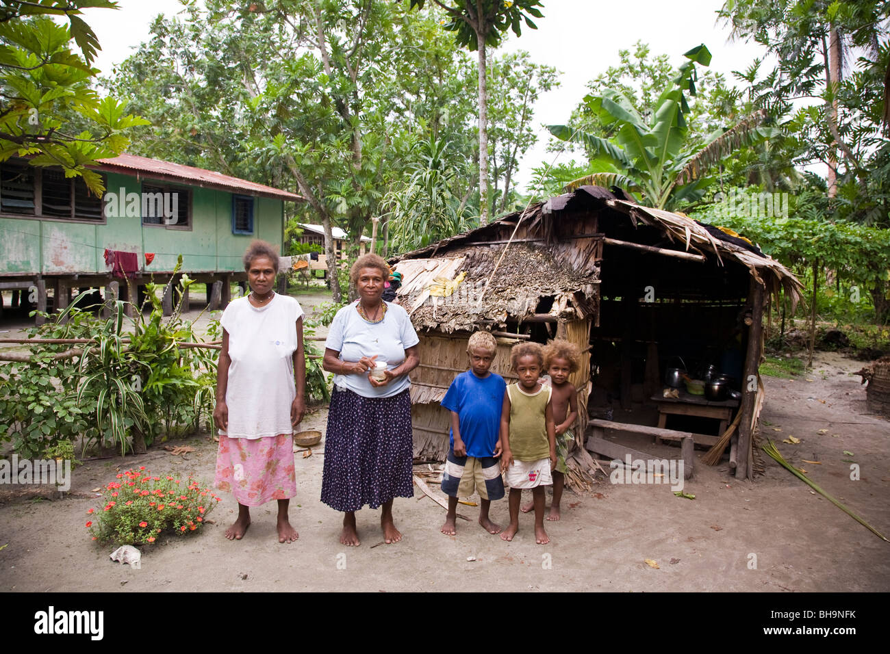 Zwei melanesische Frauen und drei melanesischen Kinder posieren für die Kamera vor einem strohgedeckten Hütte Stockfoto