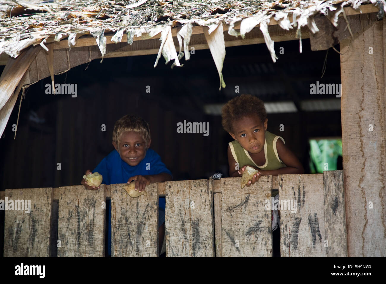 Zwei melanesische Kinder blicken in die Kamera über ein Tor in eine strohgedeckte Hütte Santa Ana Insel Melanesien Stockfoto