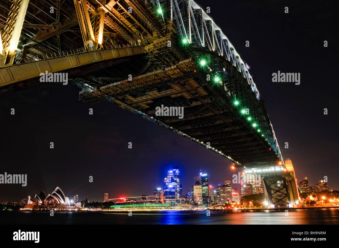 Sydney Harbour Bridge bei Nacht Sydney // SYDNEY, Australien – die beleuchtete Sydney Harbour Bridge überspannt das Wasser des Sydney Harbour bei Nacht, wobei die Skyline der Stadt eine Kulisse aus beleuchteten Gebäuden vor dem dunklen Himmel bildet. Die Aussicht, die vom Milsons Point am Nordufer erfasst wurde, blickt nach Süden in Richtung Dawes Point, wo das südliche Ende der Brücke mit der Stadt verbunden ist. Das unverwechselbare segelförmige Dach des Sydney Opera House, das 1973 zum UNESCO-Weltkulturerbe gehört, ist ganz links vom Rahmen zu sehen. Die 1932 eröffnete Sydney Harbour Bridge ist eine der bekanntesten Australiens Stockfoto