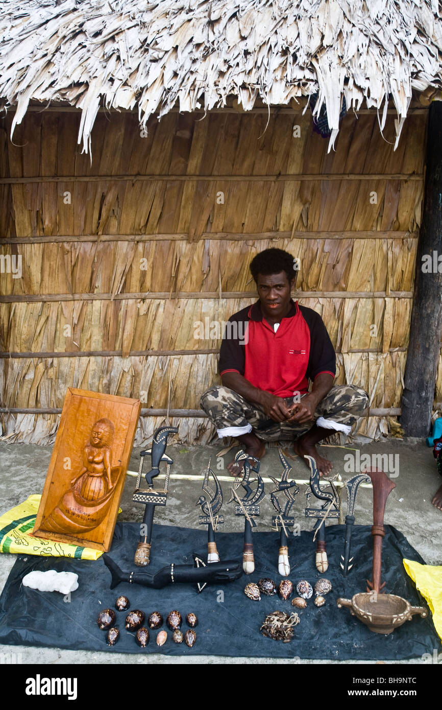 Melanesische Handwerker zeigt sein Handwerk, wie er vor eine strohgedeckte Hütte sitzt Stockfoto