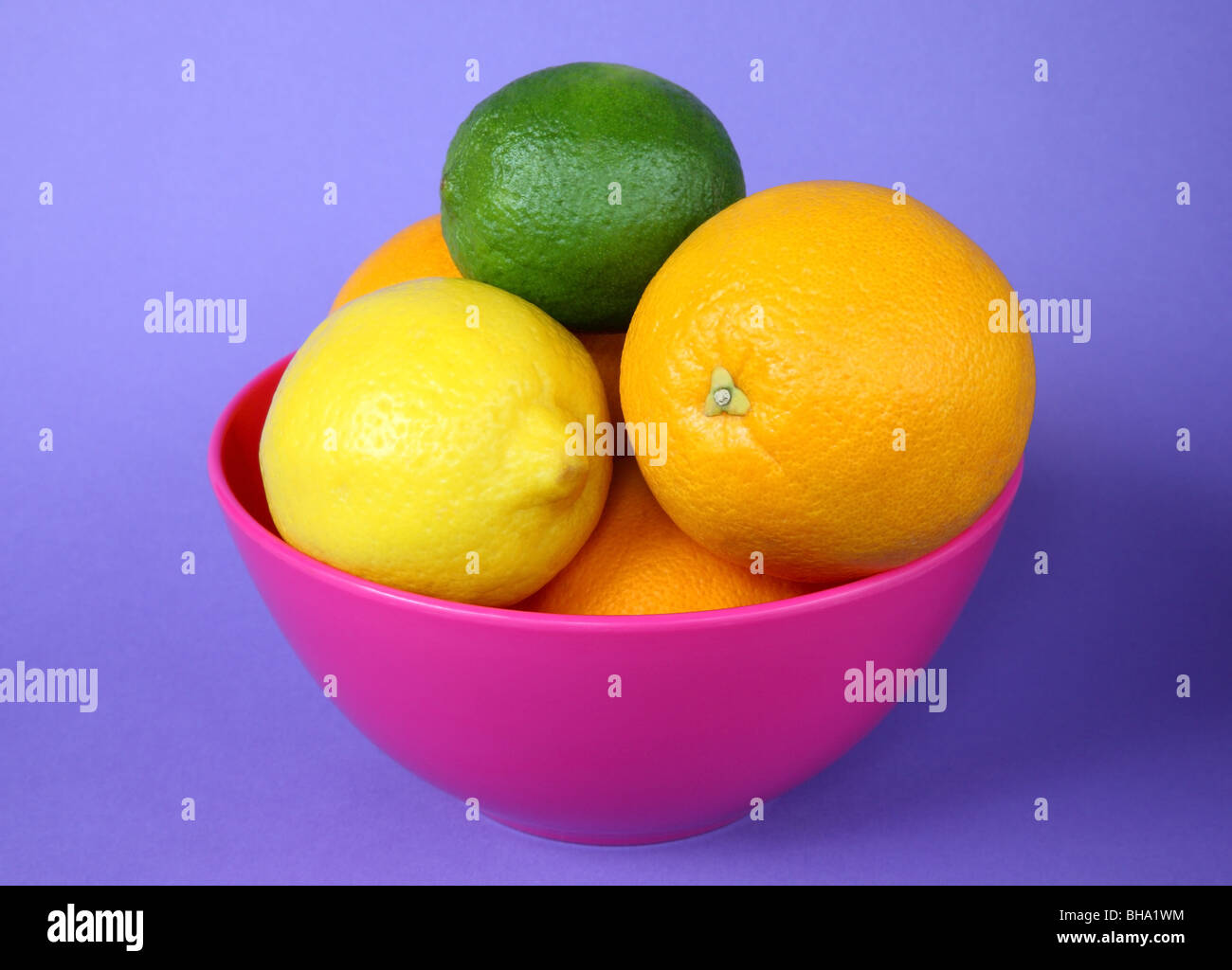 Hell rosa Schale gefüllt mit Orangen, Zitronen und Limetten, auf lila Hintergrund Stockfoto