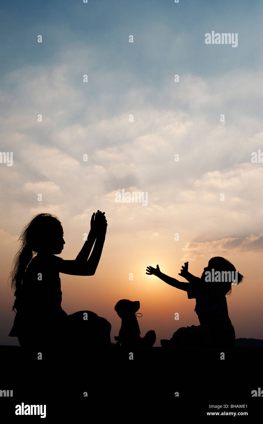 Silhouette von einem indischen Mädchen mit einem Teddy bear klatschenden Händen dort bei Sonnenuntergang. Indien Stockfoto