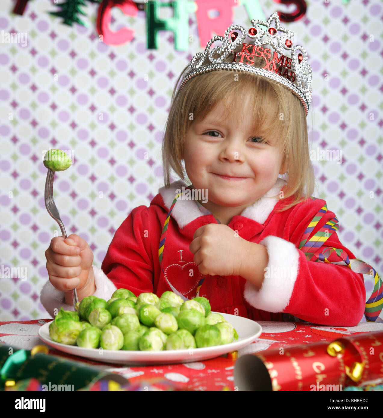 Ein nettes drei Jahre alten Mädchen mit einem Teller voller Sprossen und auf ihre Gabel am Weihnachtstisch sitzen. Stockfoto