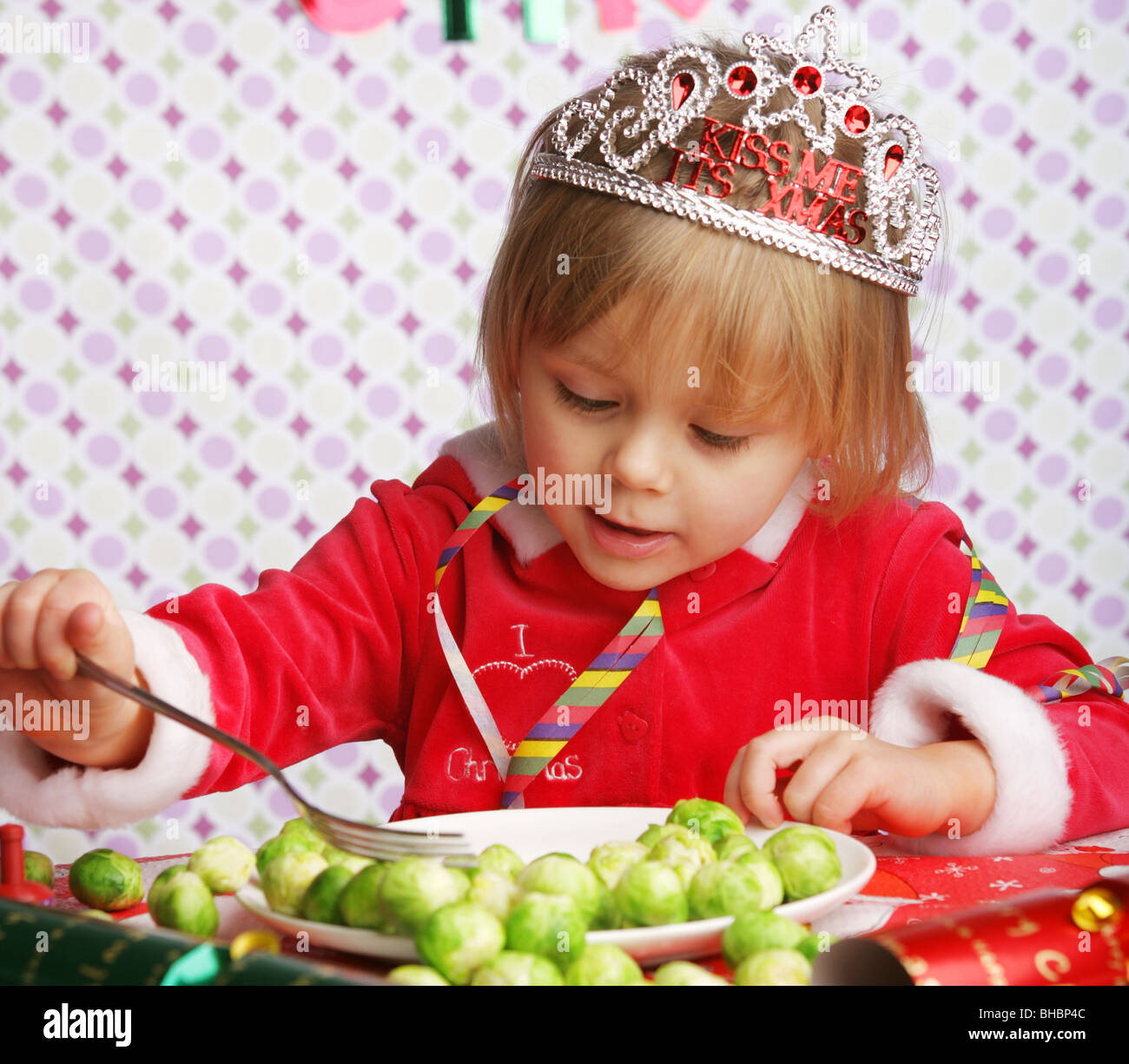 Eine drei Jahre alte sitzen an einem Tisch mit Weihnachtsschmuck und einem Teller voller Sprossen. Stockfoto