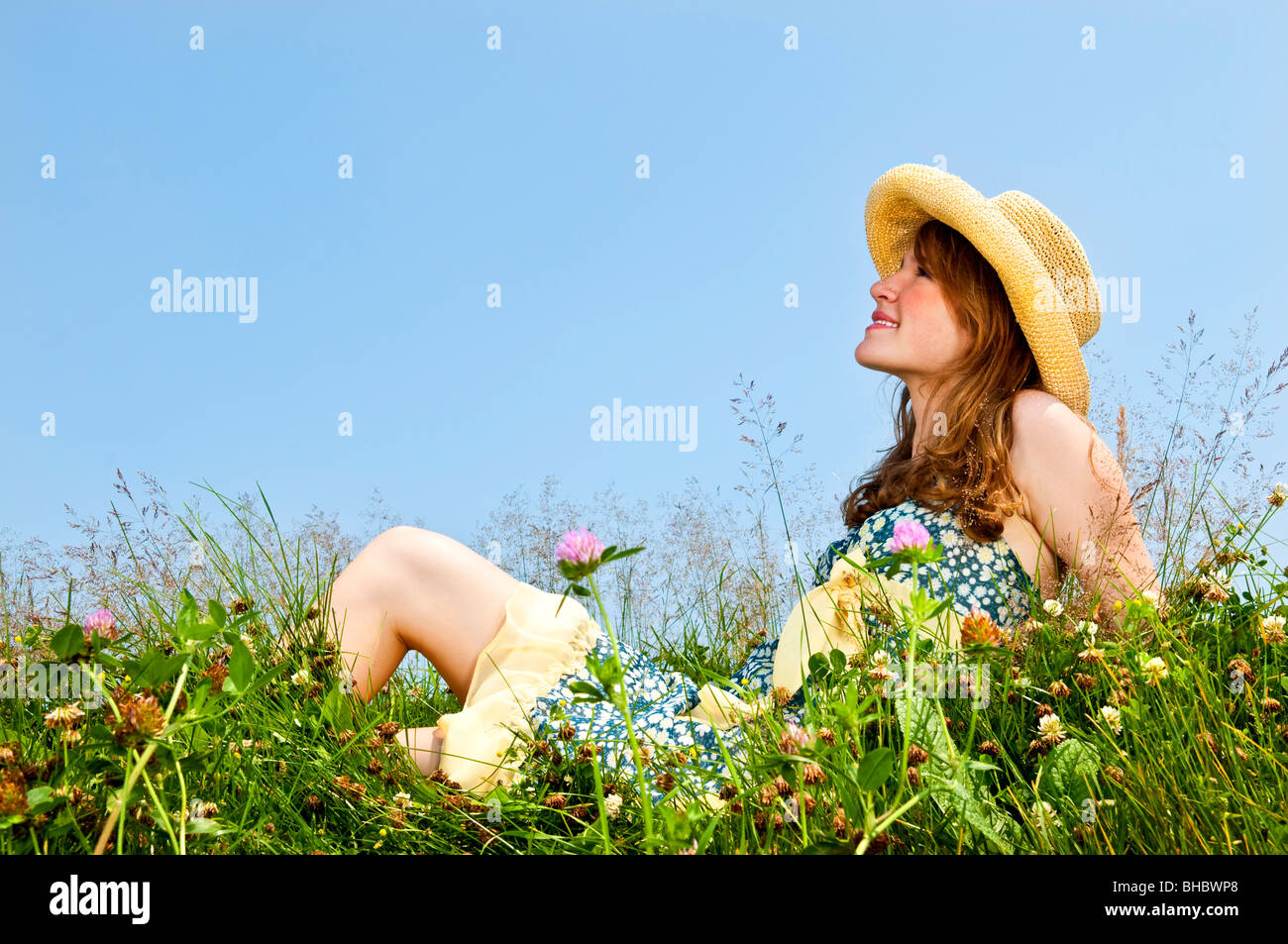 Junge Teenager-Mädchen sitzen auf Sommerwiese im Strohhut Stockfoto