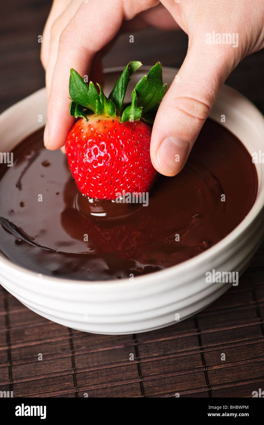 Hand, die frischen Erdbeere in geschmolzene Schokolade eintauchen Stockfoto