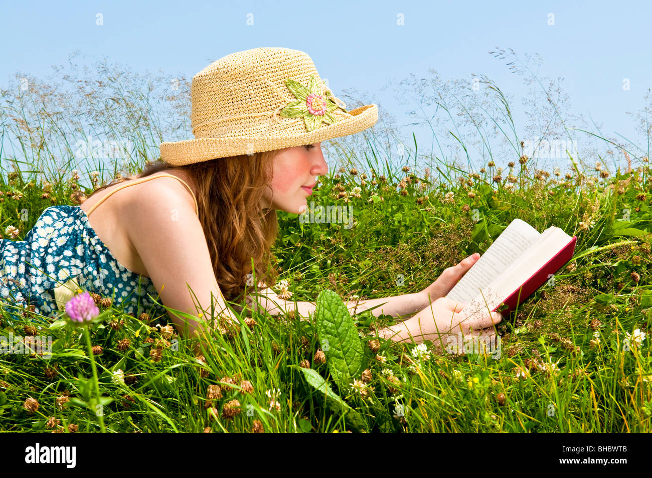 Junge Teenager-Mädchen-Lesebuch in Sommerwiese mit Strohhut Stockfoto