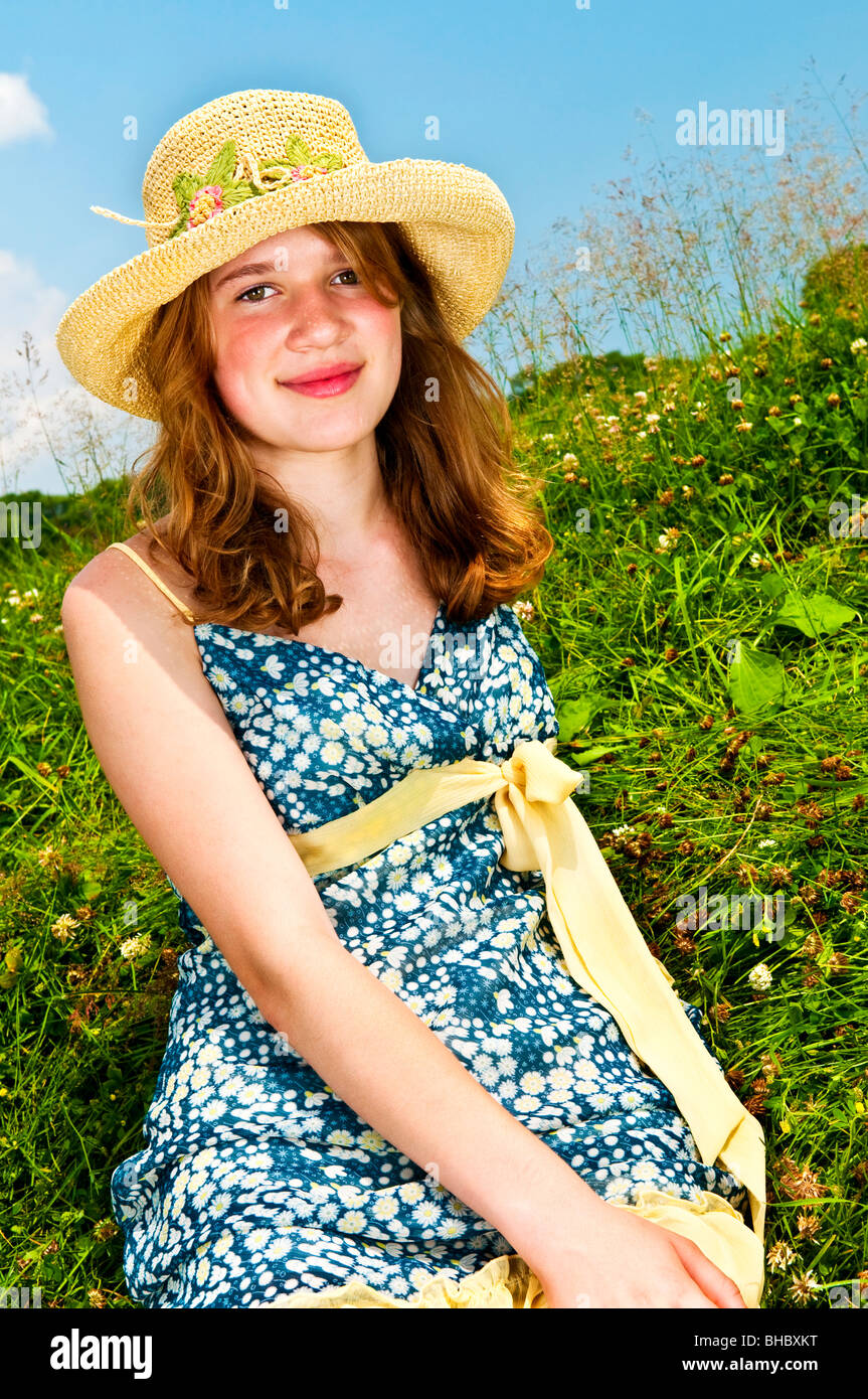 Junge Teenager-Mädchen sitzen auf Sommerwiese im Strohhut Stockfoto