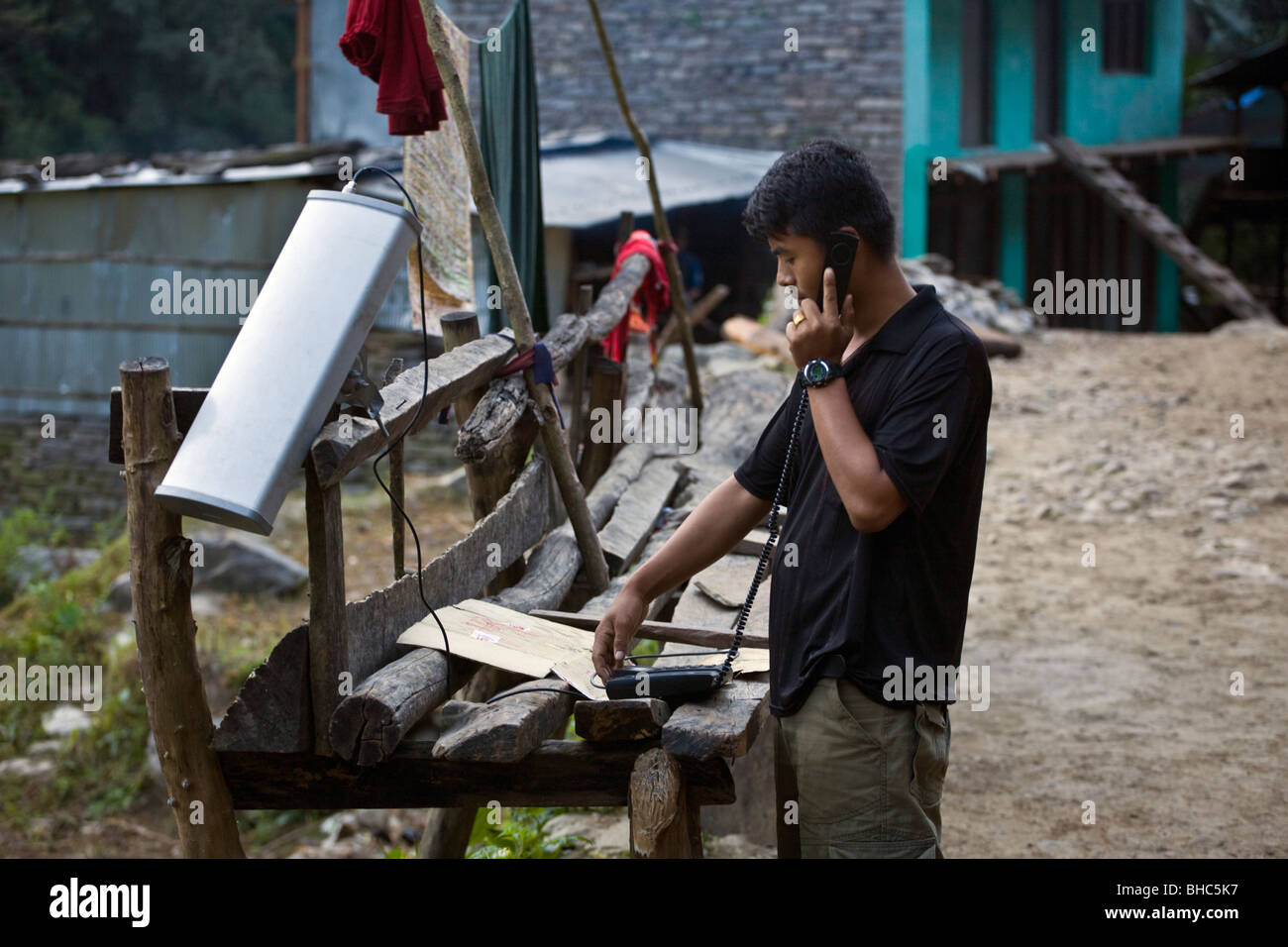 Ein Mann nutzt ein SOLAR Handy in einem abgelegenen Dorf entlang der Bhudi Ghandaki Schlucht - um MANASLU Trekking, NEPAL Stockfoto