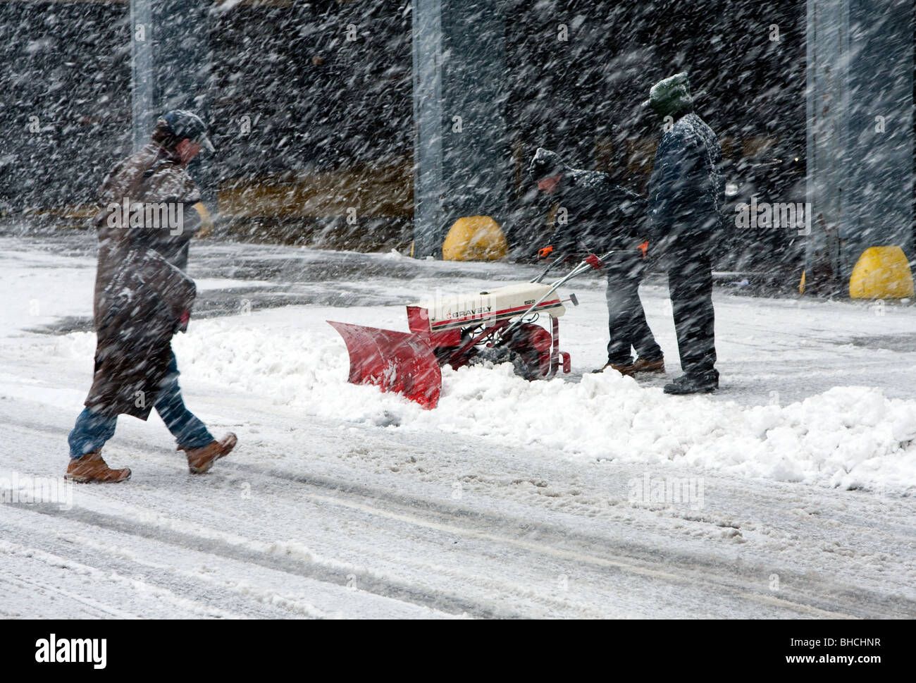 Zwei Männer Schnee Schaufeln mit einer automatischen Pflug während Mann ist Fuß über die Straße bei starkem Schneefall in schlechtem Wetter Bli fallen Stockfoto