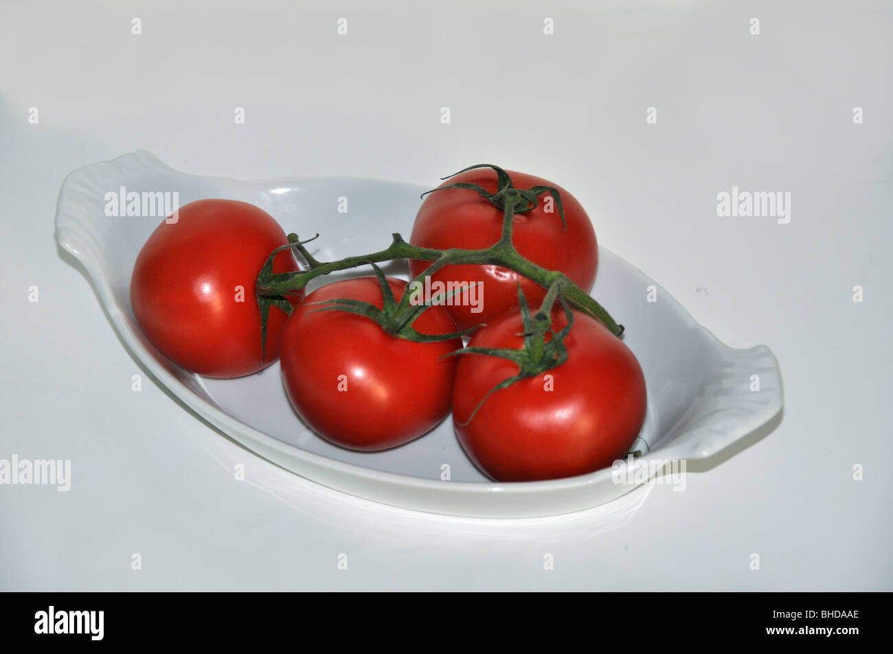 4 reife Tomaten am Rebstock in eine weiße ovale Schale Stockfoto