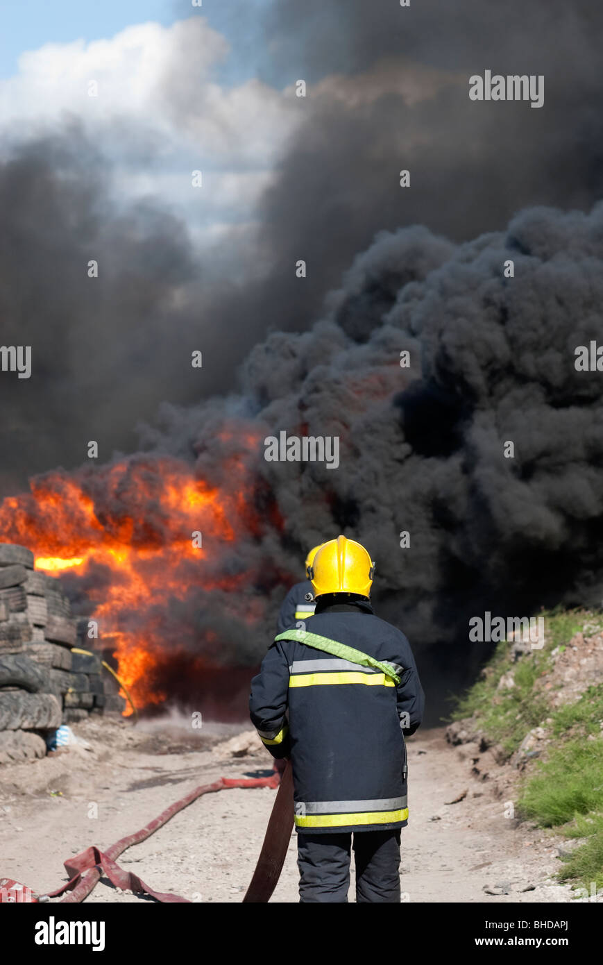 Feuerwehrmann zu Fuß in Richtung dicke schwarze Rauchfahne und Feuer Stockfoto