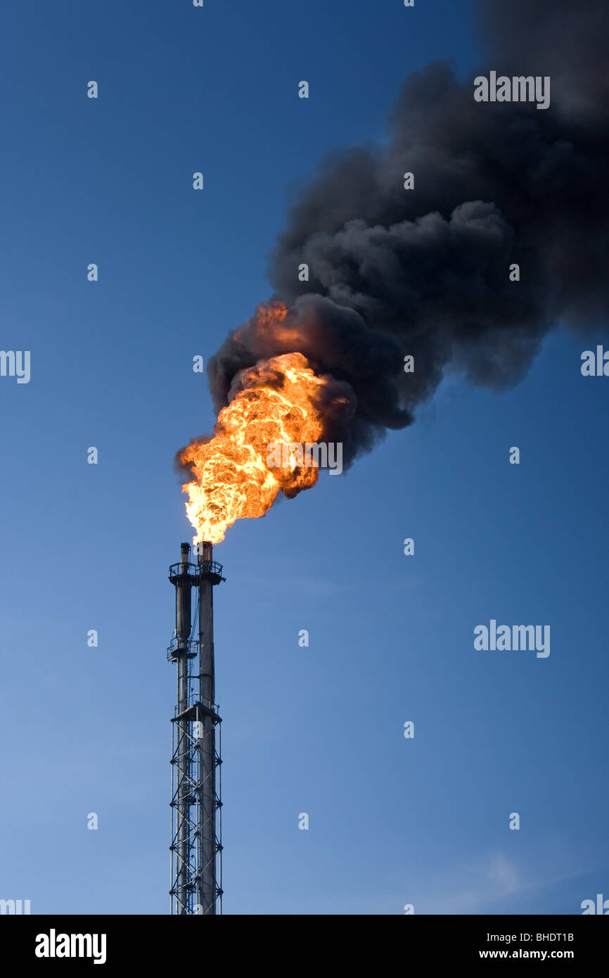 Raffinerie-Trichter mit großer Flamme brennen und werfen dunkle Rauchwolken Stockfoto