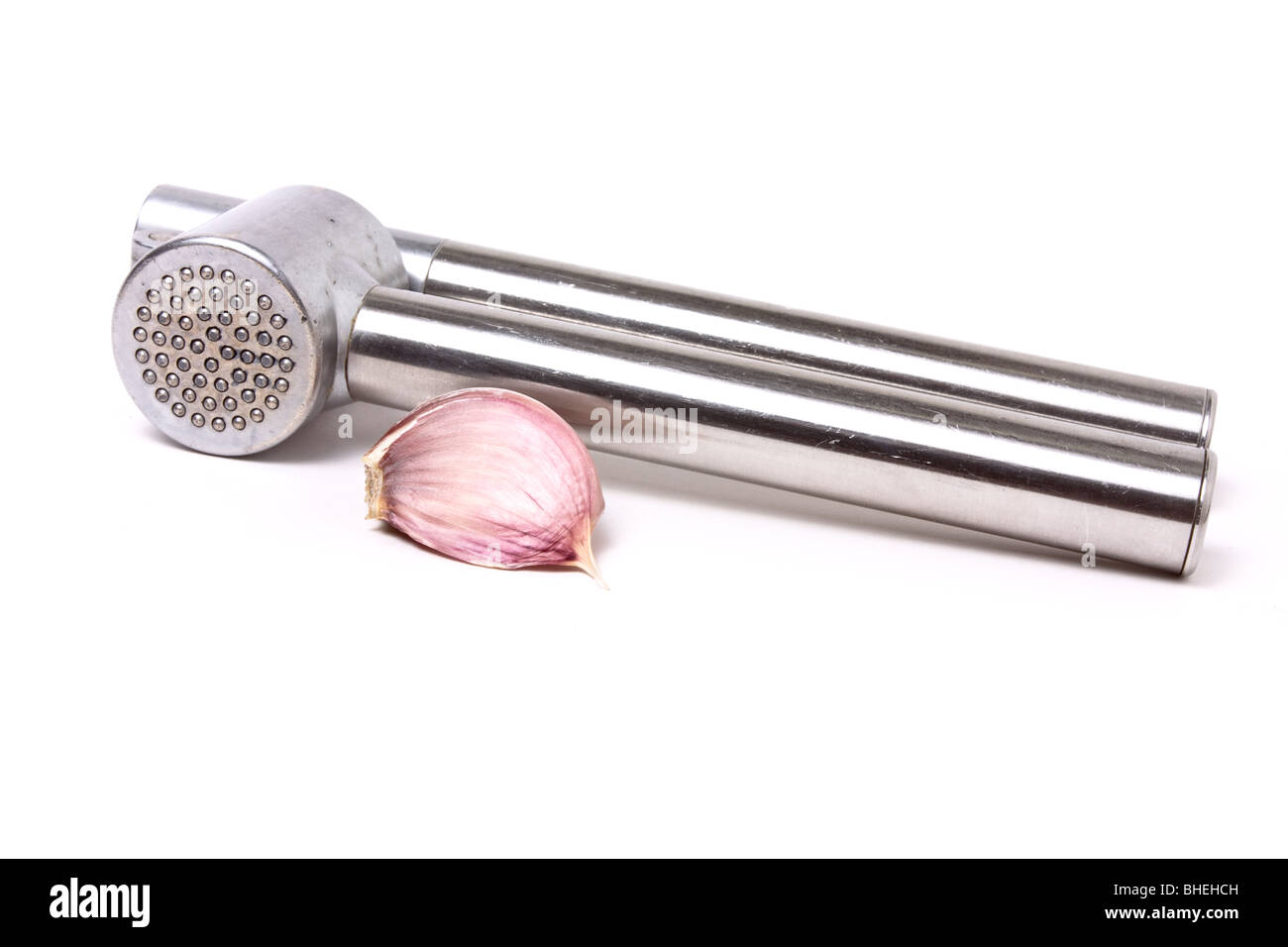 Nahaufnahme der Knoblauchzehe neben einer glänzenden Silber Knoblauchpresse isoliert vor weißem Hintergrund. Stockfoto
