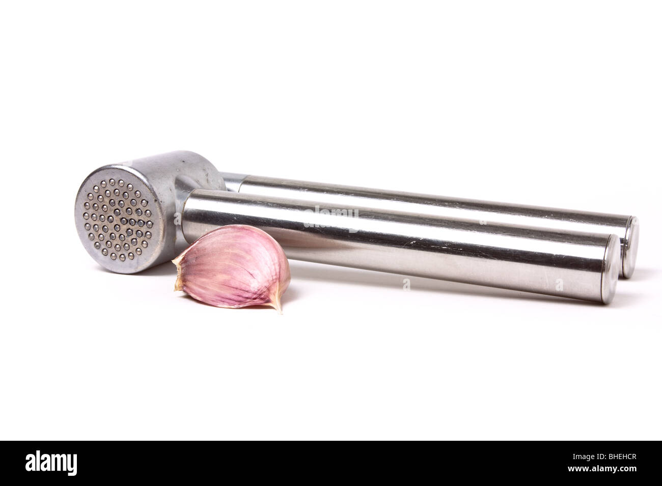 Nahaufnahme der Knoblauchzehe neben einer glänzenden Silber Knoblauchpresse isoliert vor weißem Hintergrund. Stockfoto
