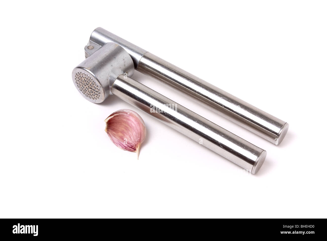 Nahaufnahme der Knoblauchzehe neben einer glänzenden Silber Knoblauchpresse isoliert vor weißem Hintergrund. Stockfoto