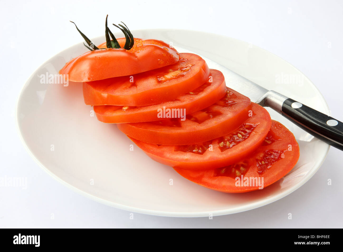 Eine rote, Reife, saftige Rindfleisch Tomaten in sechs Scheiben schneiden, mit Messer auf weißen Teller mit weißem Hintergrund. Stockfoto