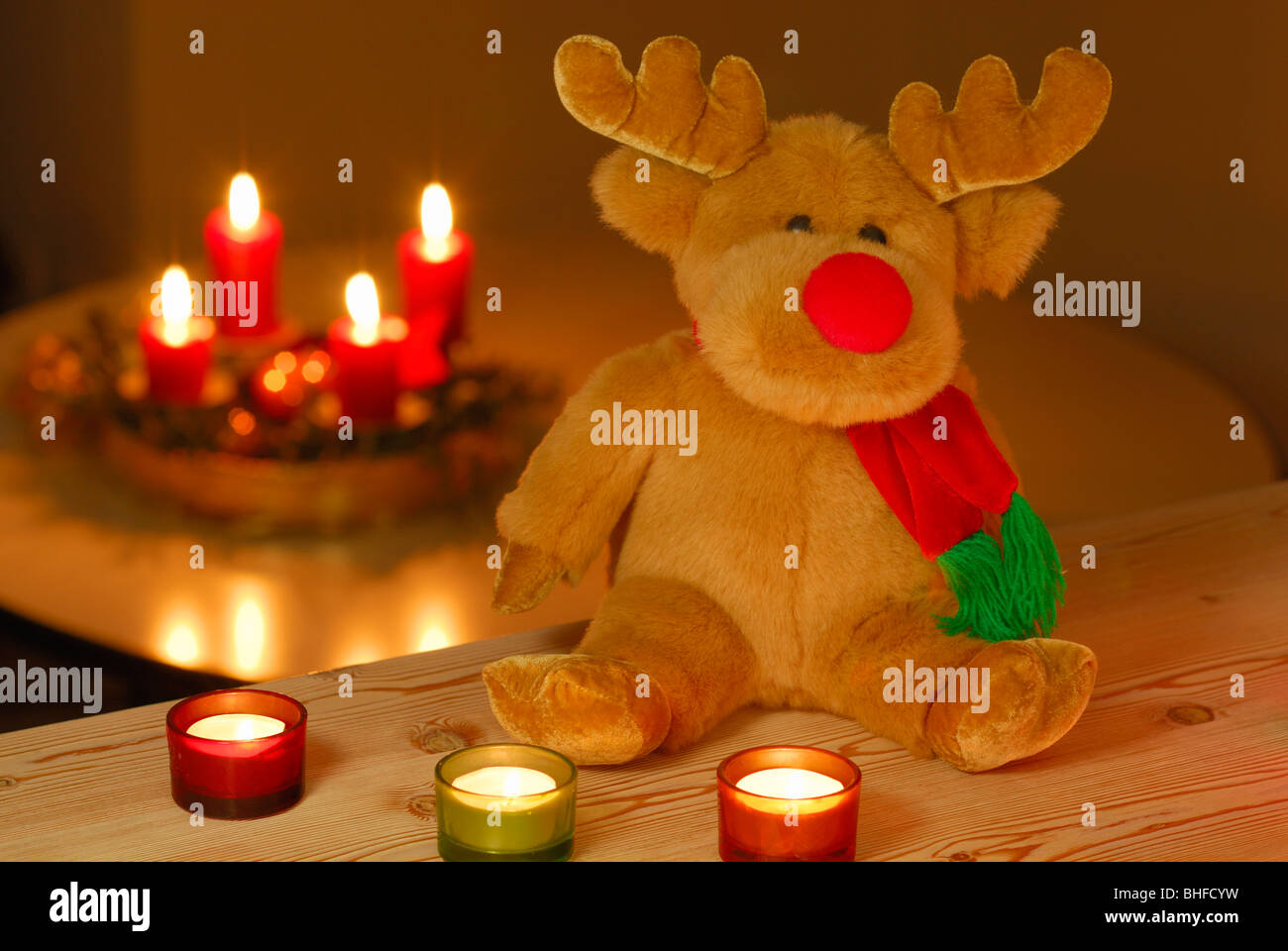 Rudolph die Red-Nosed Reindeer als ausgestopfte Tier sitzen vor brennenden Kerzen, mit Adventskranz im Hintergrund Stockfoto