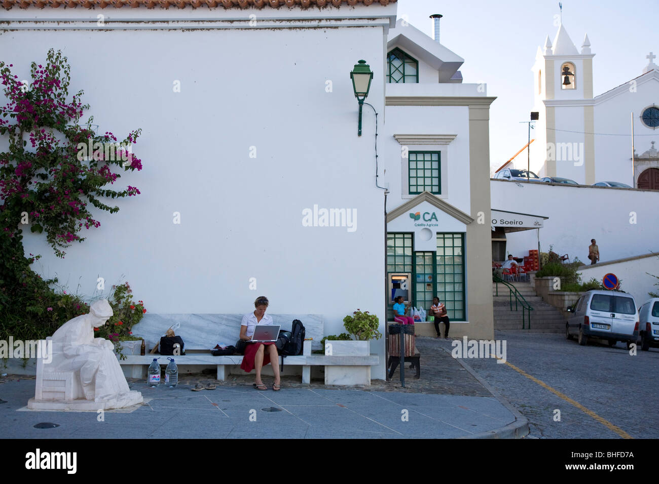 Yong Frauen mit ihrem Laptop, Notebook, mit kostenlosem Internetzugang, W-LAN, weiße Kirche und Dorfplatz, Alcoutim, Algarve, Po Stockfoto