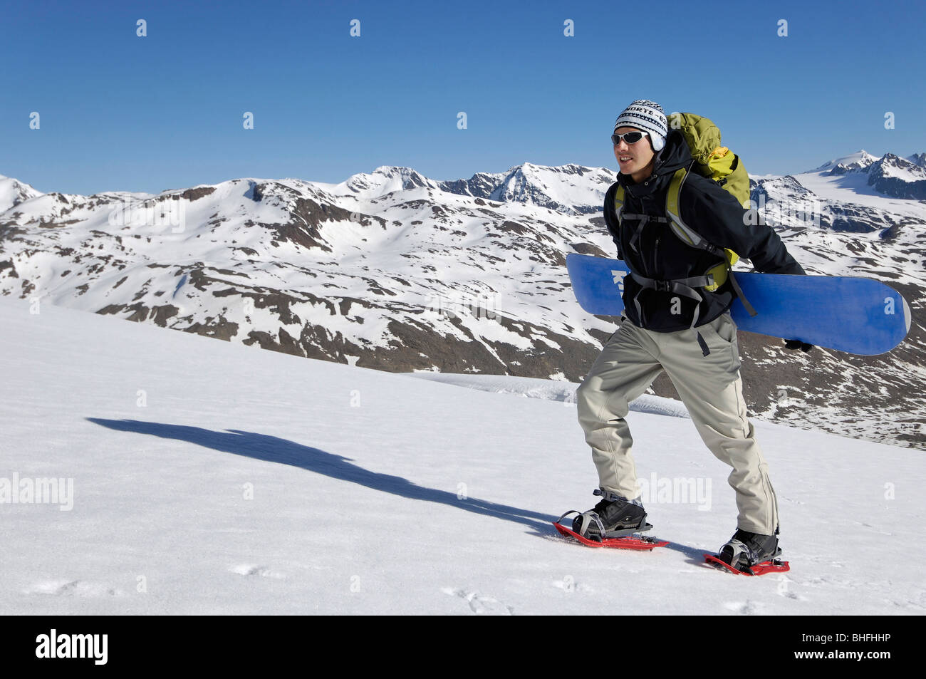 Snowboarder mit Snowboard am Aufstieg unter blauem Himmel, Schnals Tal, Val Venosta, Südtirol, Italien, Europa Stockfoto