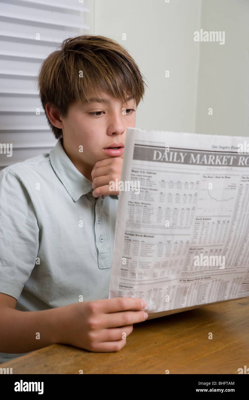 14 Jahre Alter Koreanisch/weiß Junge liest den Finanzteil der LA Times beim Sitzen am Küchentisch. Stockfoto