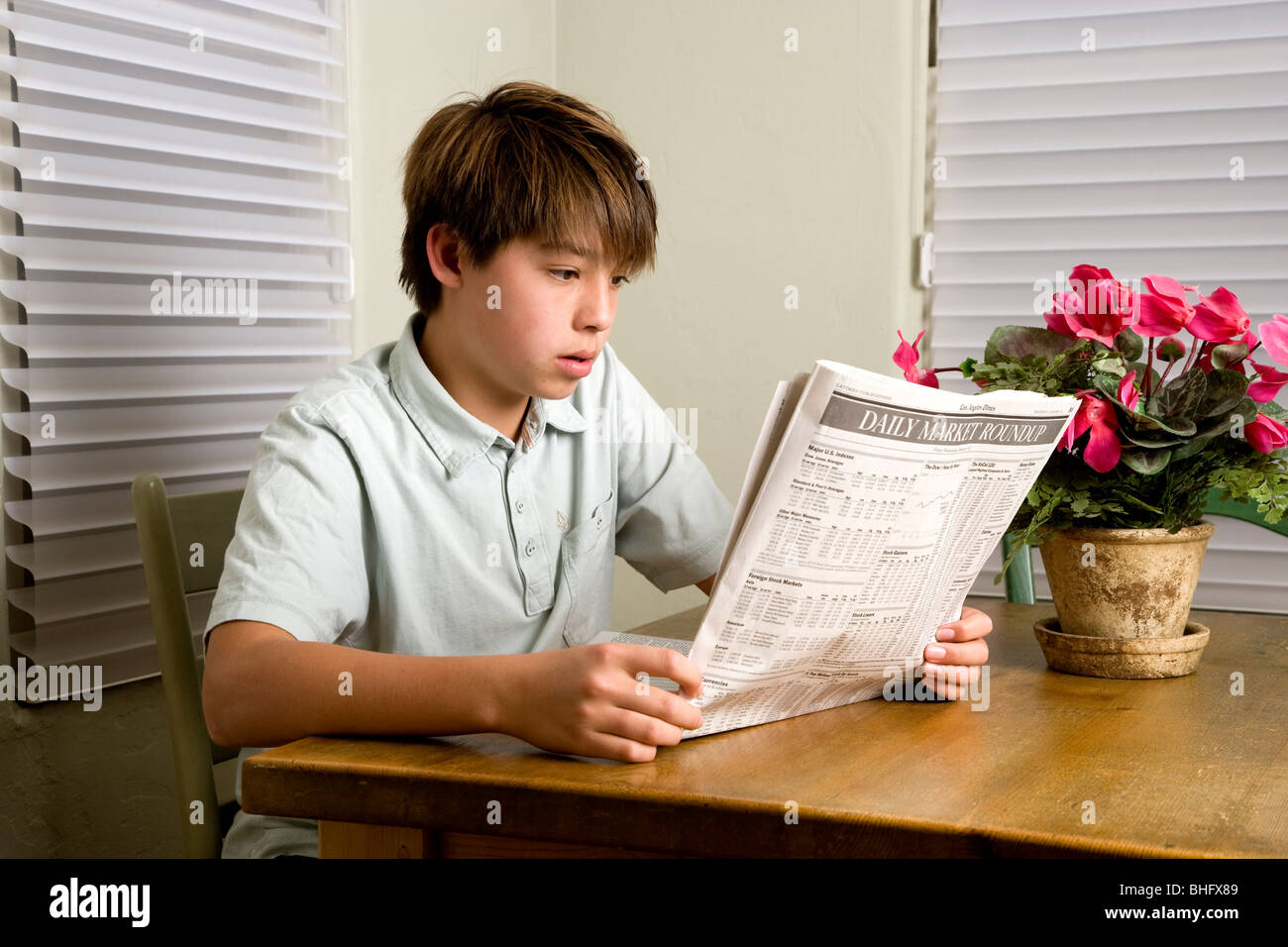 14 Jahre Alter Koreanisch/weiß Junge liest den Finanzteil der LA Times beim Sitzen am Küchentisch. Stockfoto