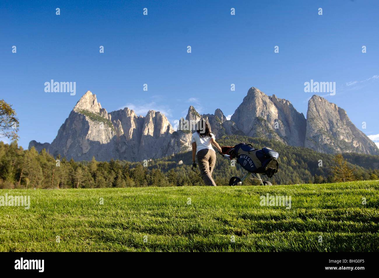 Frau mit Golf-Bag auf der Wiese unter blauem Himmel, Golfplatz Kastelruth-Seiser, Schlern, Südtirol, Italien, Europa Stockfoto