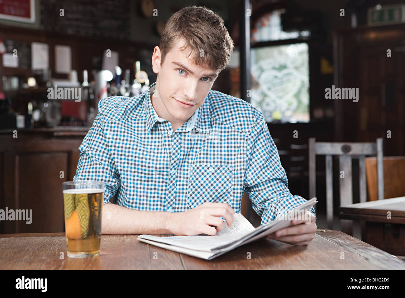 Junger Mann Bar mit Zeitung und Bier Stockfoto