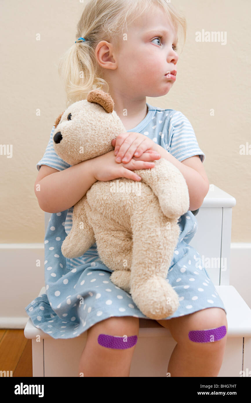 Mädchen mit Teddybär und Putze auf Knien Stockfoto