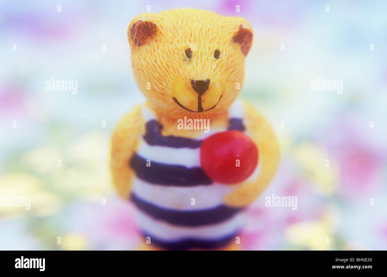 Kleinen Volumenmodell des Lächelns gelber Teddybär in gestreiften Badeanzug halten rote Kugel stehend auf Hintergrund von Pastellfarben Stockfoto