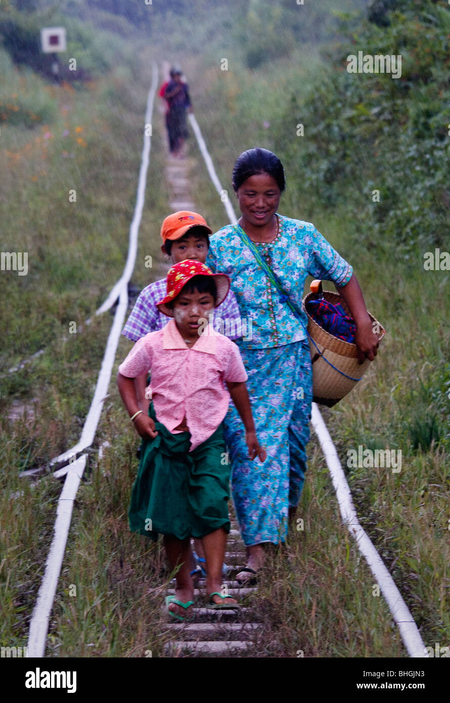 Eine Frau mit ihren beiden Kindern zu Fuß entlang einem verbeulten Gleis zum Bahnhof im Regen, im Nord-östlichen Myanmar Stockfoto