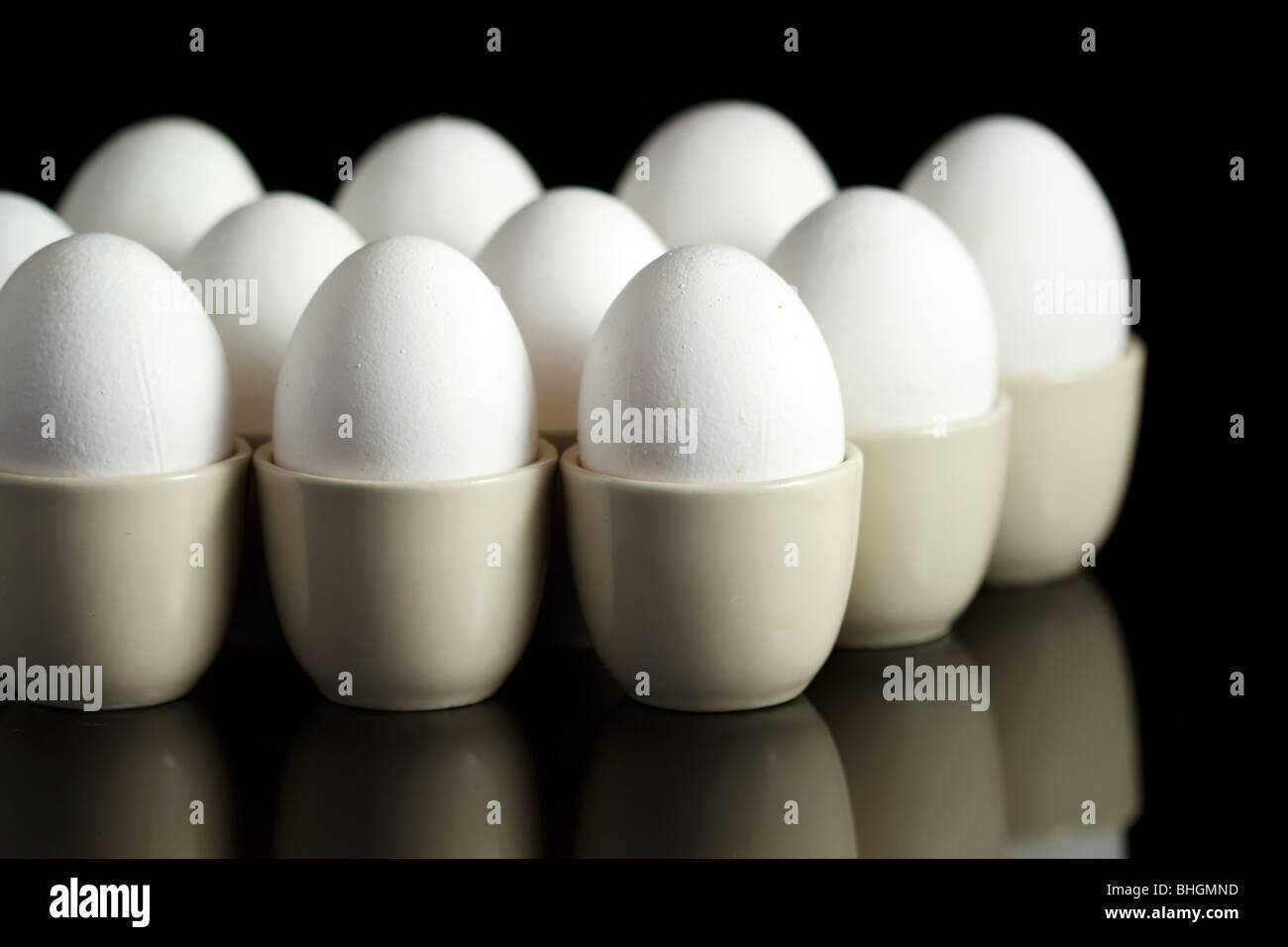 weiße Hühnereier in Eierbecher auf schwarzem Hintergrund reflektiert Stockfoto