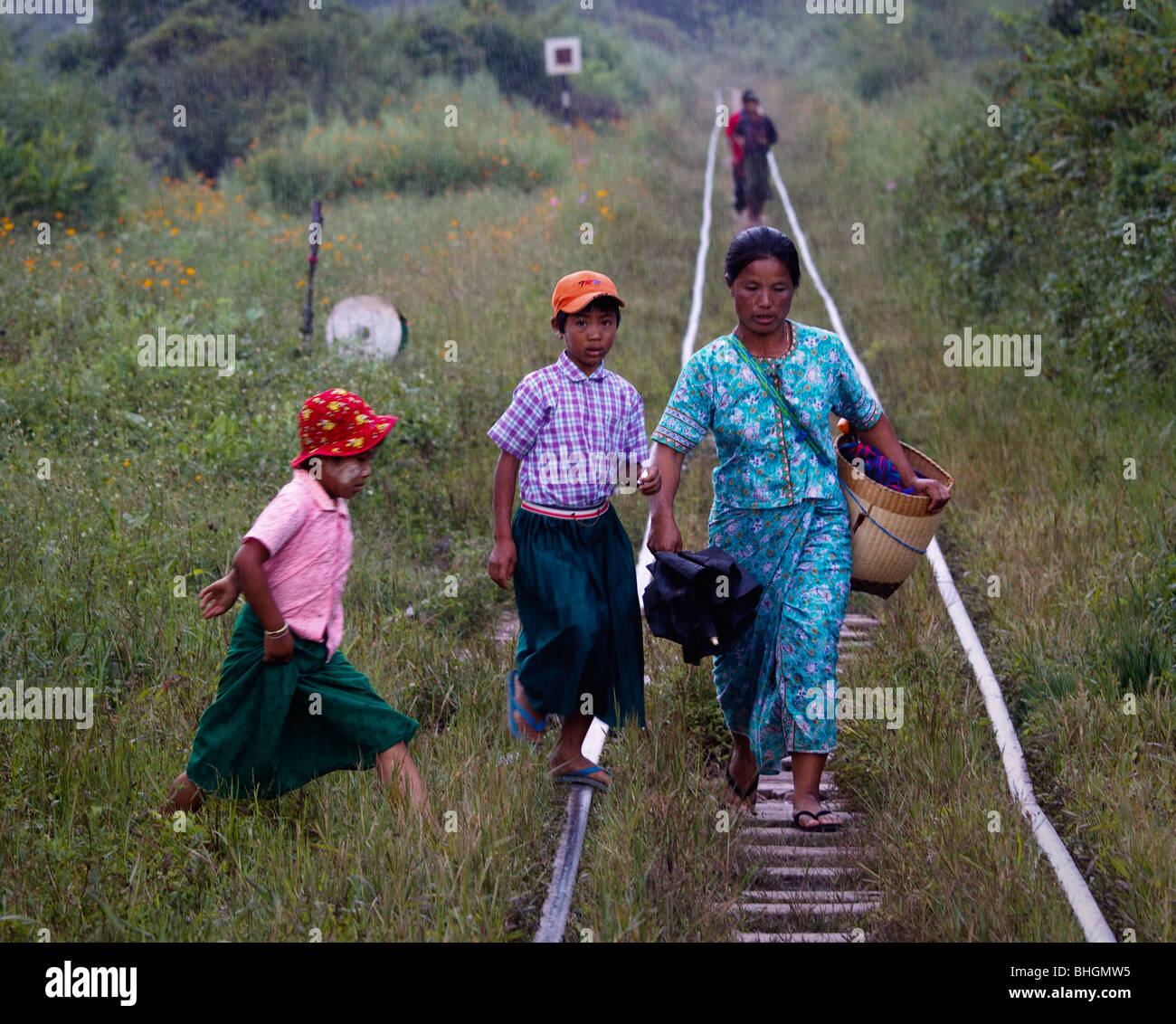 Eine Frau mit ihren beiden Kindern zu Fuß entlang einem verbeulten Gleis zum Bahnhof im Regen, im Nord-östlichen Myanmar Stockfoto