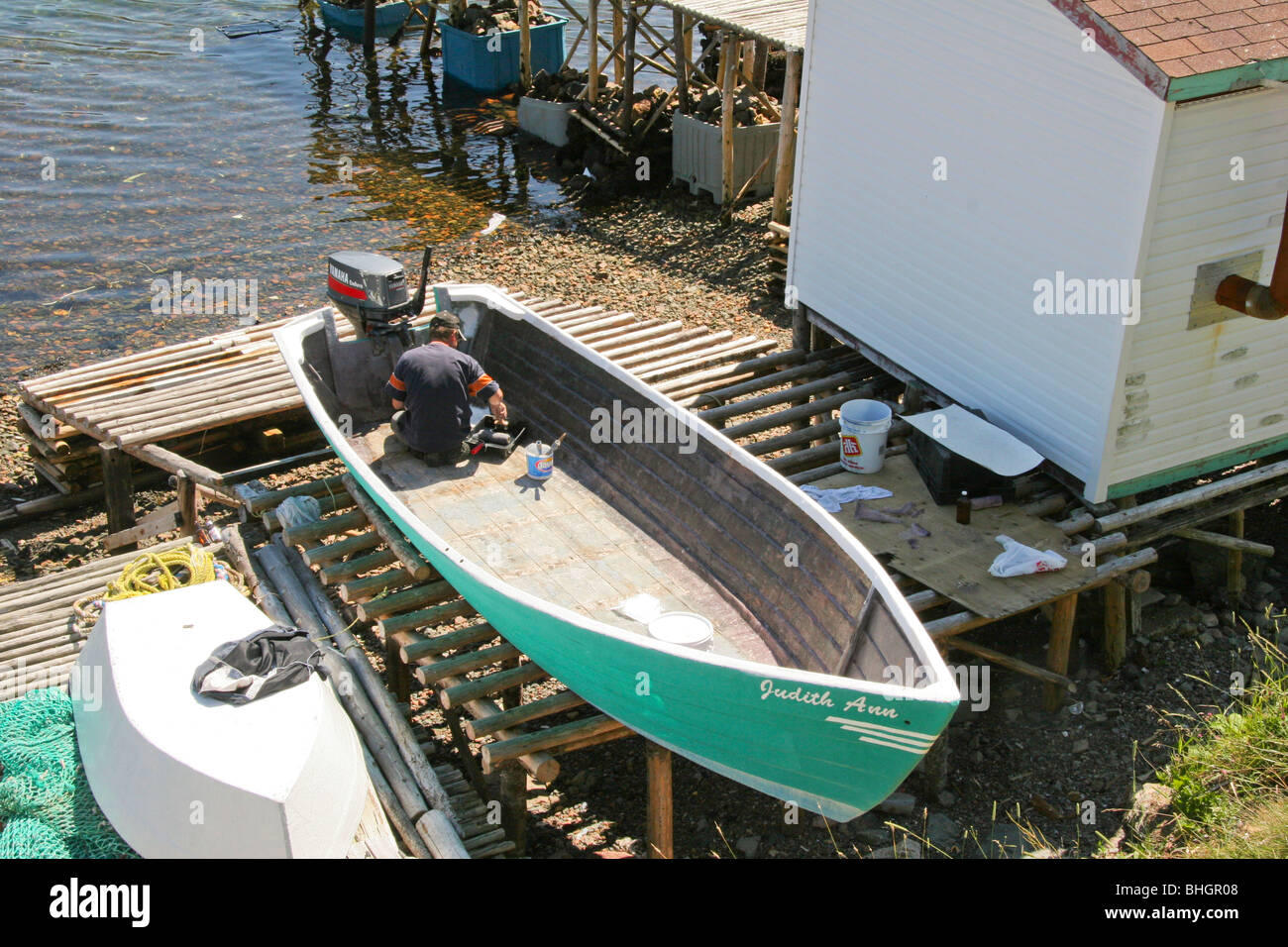 Ein Mann rollt Farbe auf der Innenseite von seinem Skiff am Ufer am Harbour Breton, Neufundland Stockfoto