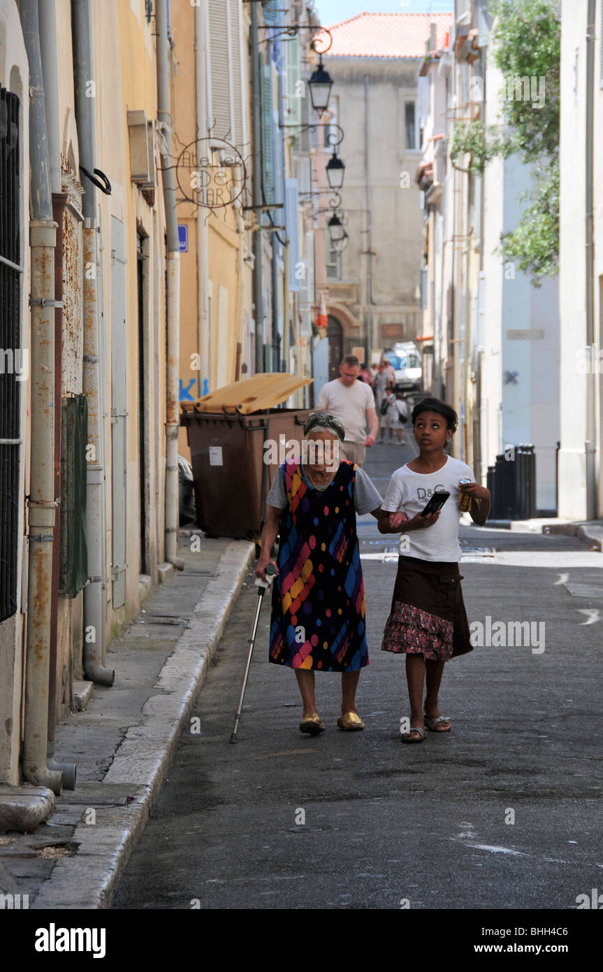 Ein junges Mädchen unterstützt eine alte Frau auf einer Straße in Marseille Stockfoto