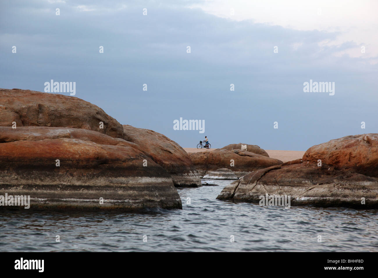 Eine lokale Sri Lanka mit seinem Fahrrad am Strand, zwischen den riesigen Felsen umrahmt. Lage: Pottuvil Point, Sri Lanka. Stockfoto