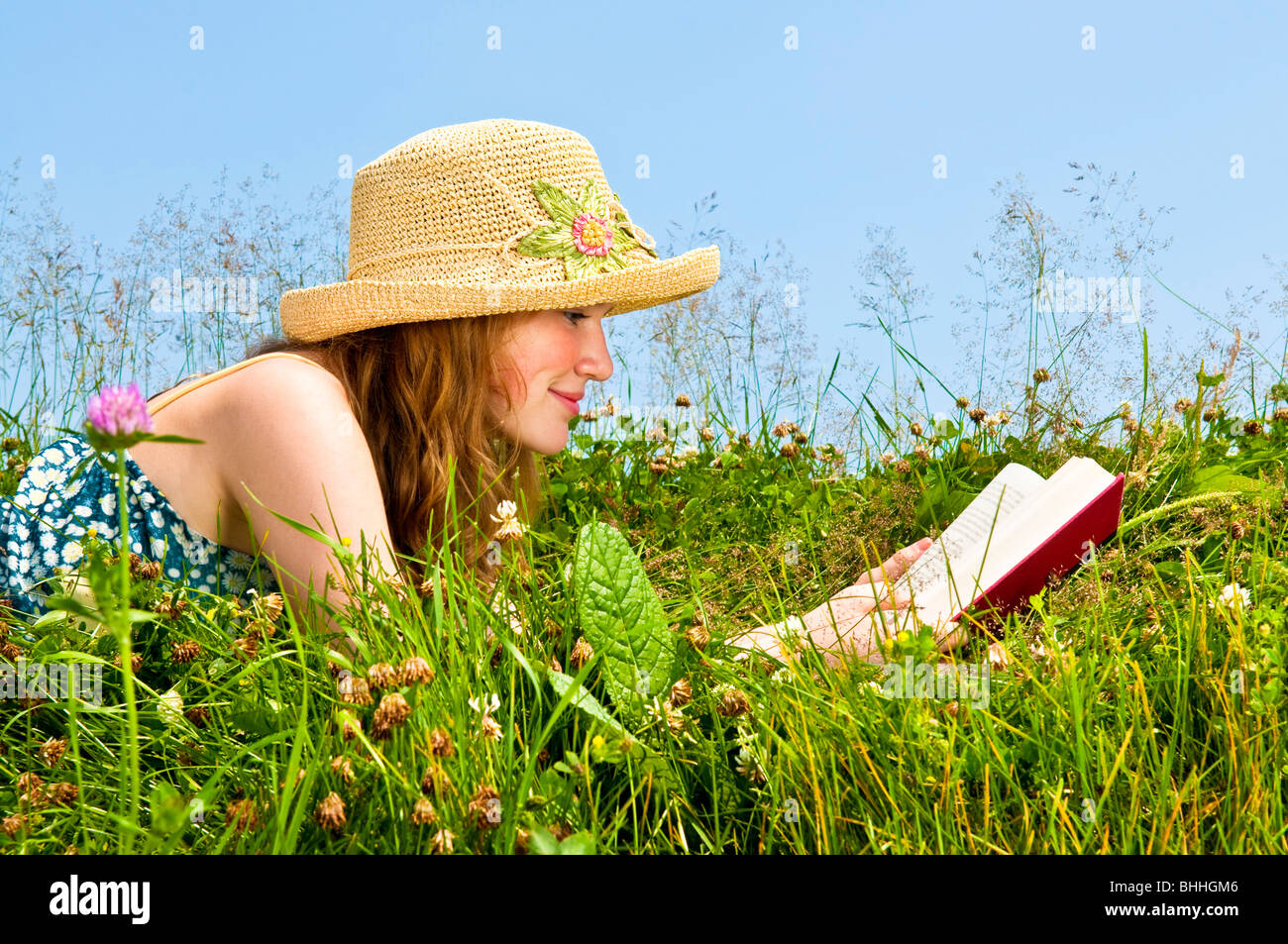 Junge Teenager-Mädchen-Lesebuch in Sommerwiese mit Strohhut Stockfoto