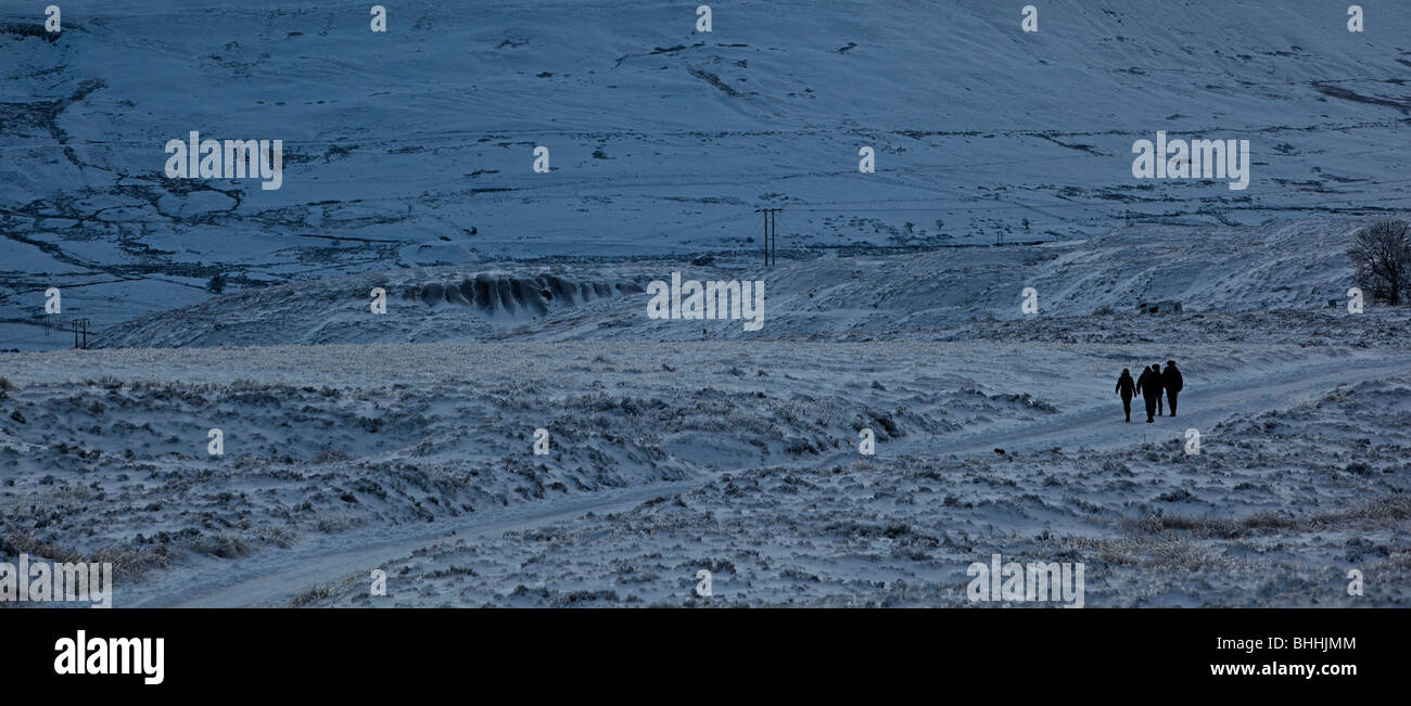 Vier Menschen zu Fuß auf verschneiten Straßen in der Abenddämmerung auf der Blorenge Heide im Winter Wales UK Stockfoto