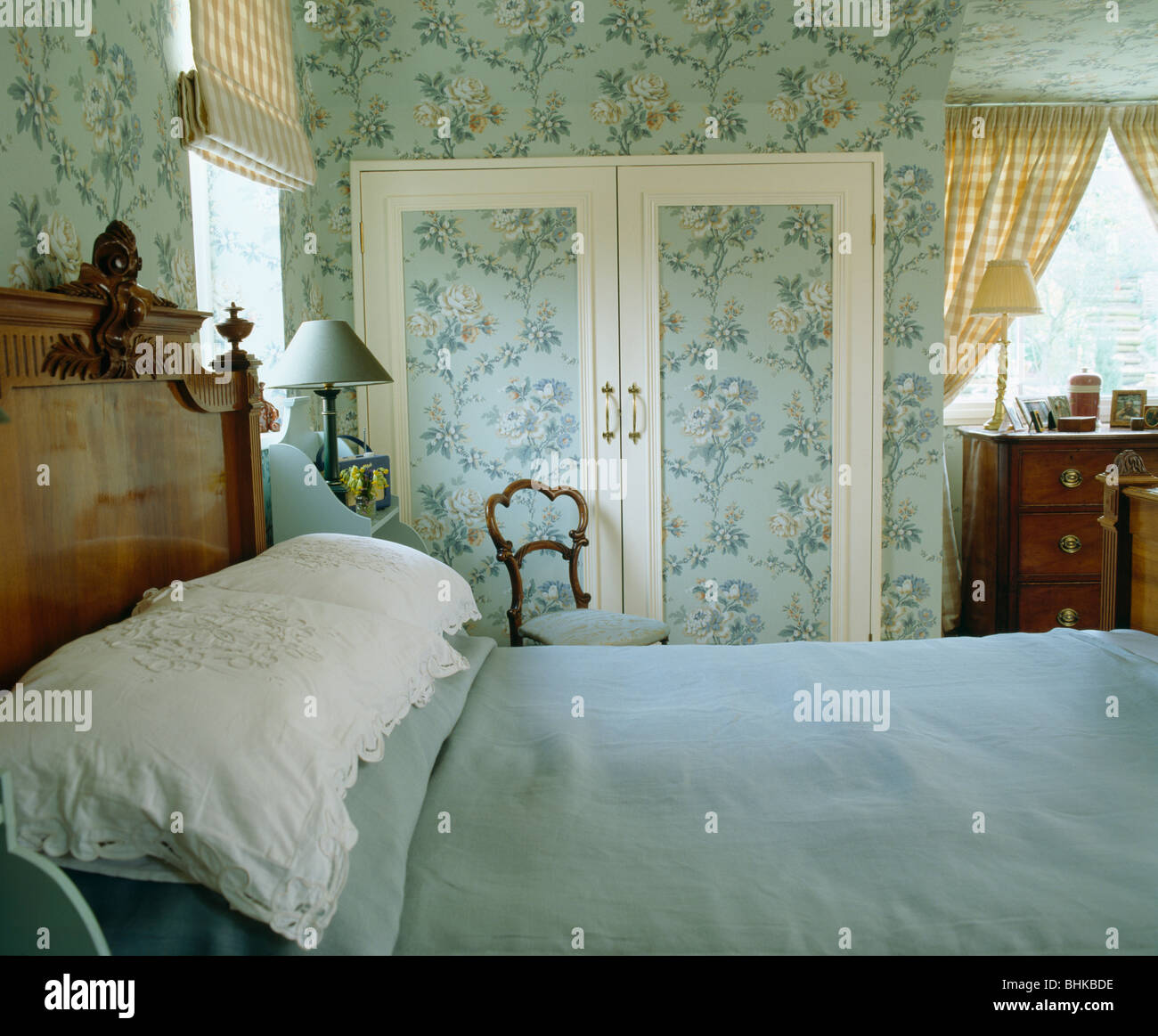 Blue floral Tapete an den Wänden und ausgestattete Schranktüren in Schlafzimmer mit blauem Leinen und weißen Kissen auf antikes Bett Stockfoto