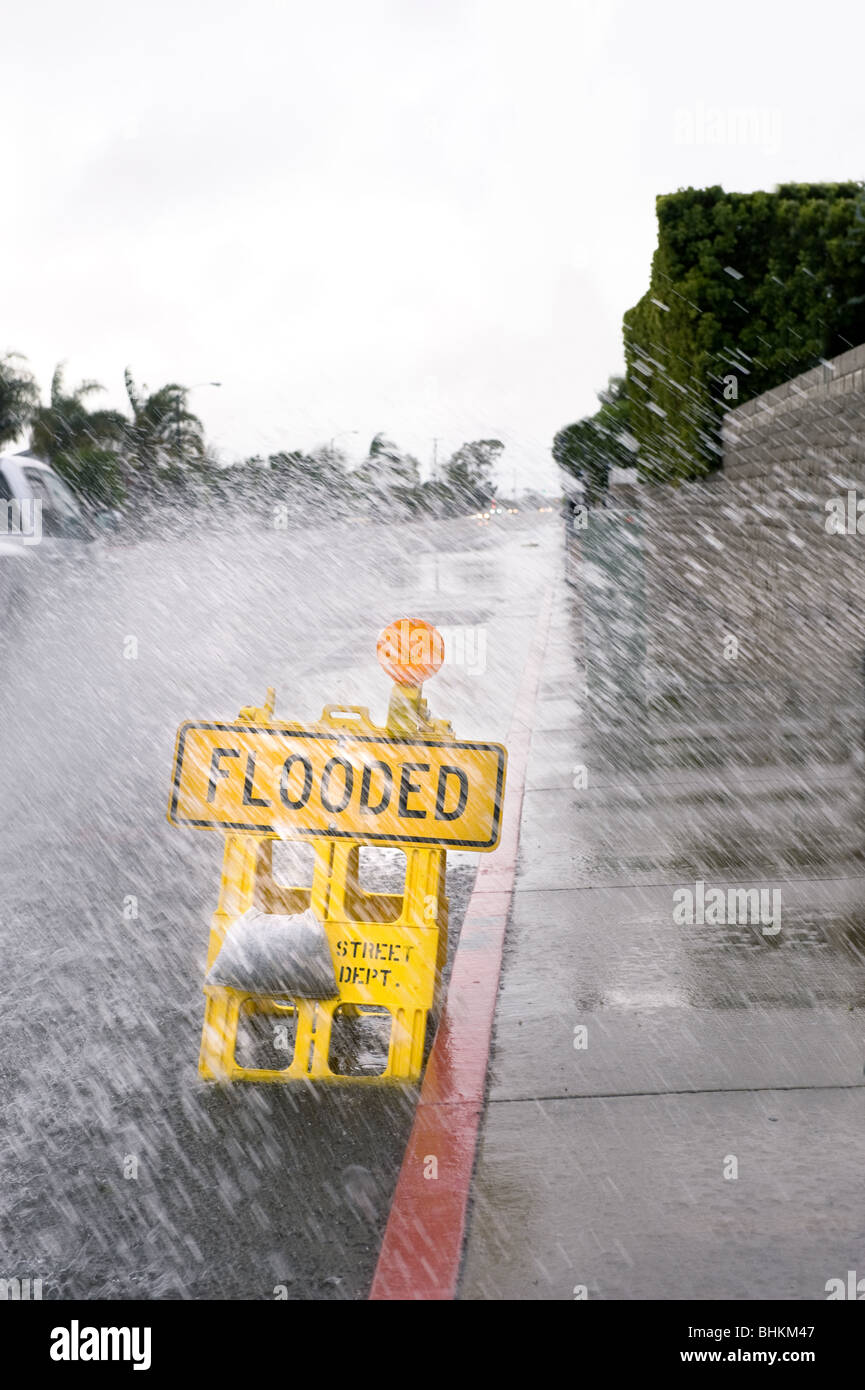 Ein Auto tritt ein Pool von Regenwasser über ein Straßenschild überflutet bei schlechtem, regnerischem Wetter. Stockfoto