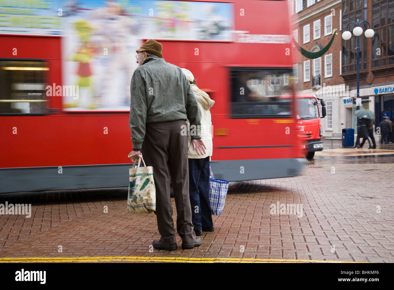 Ältere Fußgänger warten auf einen Bus vor dem Überqueren der Straße im Regen, Kingston, Surrey, England übergeben. Stockfoto