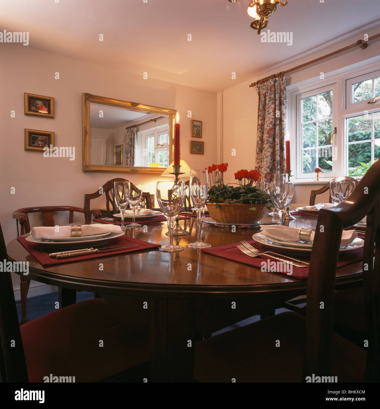 Rechteckige vergoldete Spiegel im traditionellen Speisesaal mit Weingläser und Gedecke auf Tisch mit Schale der roten cyclamen Stockfoto