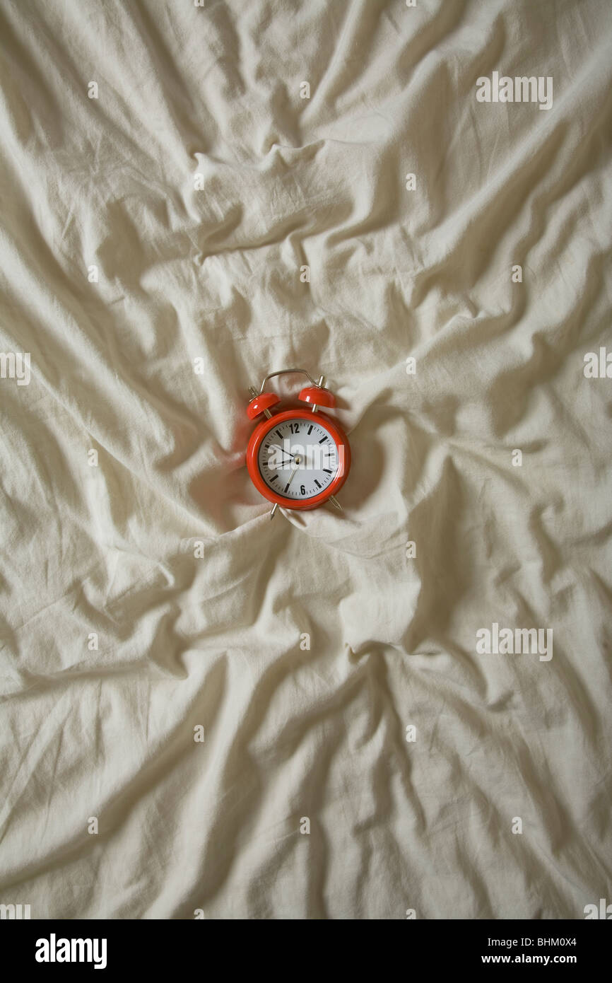 Roter Wecker zentriert auf eine faltige Bettdecke Stockfoto